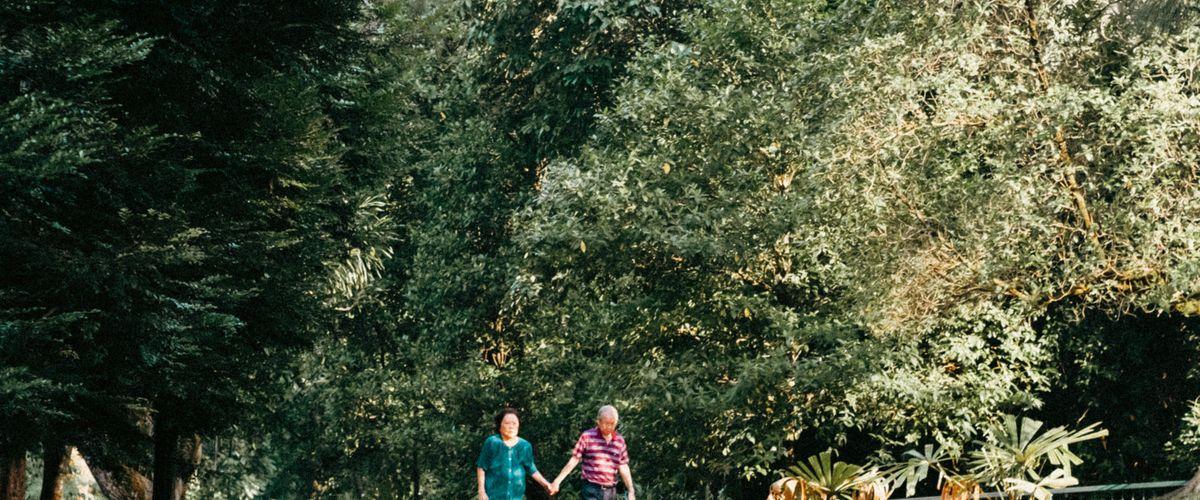 An elderly couple walking together on a beach at golden hour